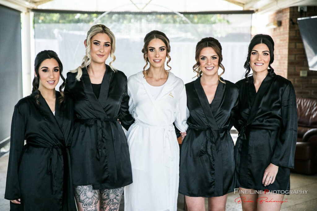 A bride with styled hair with her 4 bridesmaids in black dresses