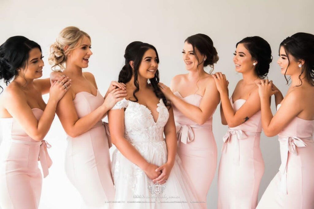 A bride with professionally styled hair surrounded by 5 bridesmaids in pink dresses